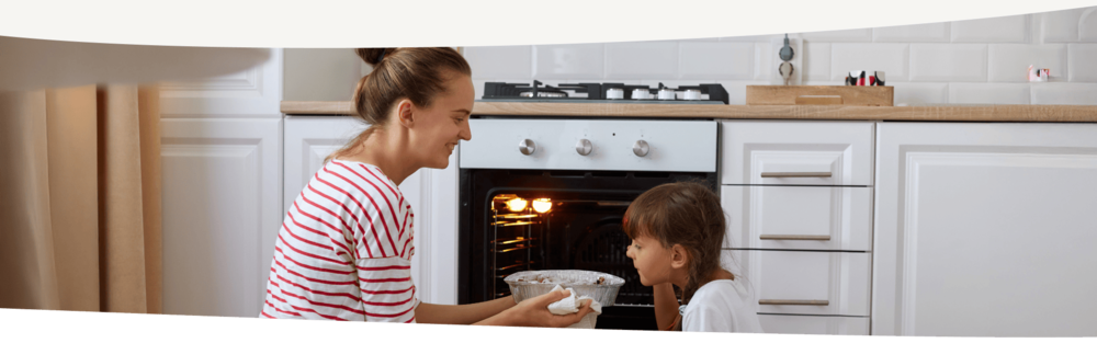 Mutter und Tochter knien vor dem Backofen und prüfen, ob der Kuchen fertig ist