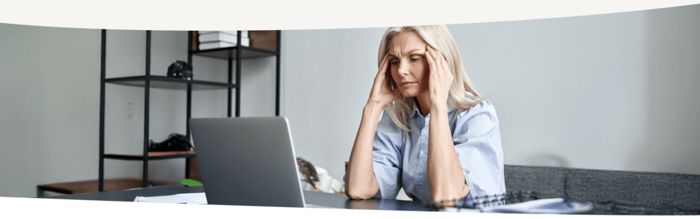 Frau in den Wechseljahren sitzt vor dem Laptop und hält sich gestresst die Hände an die Schläfe
