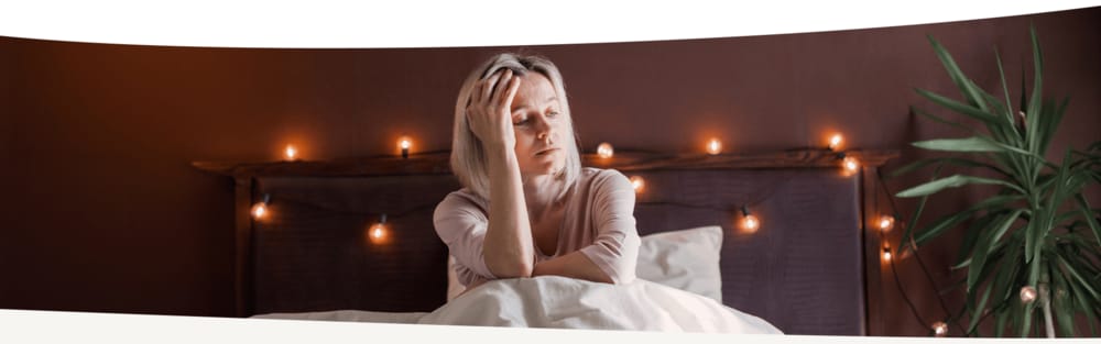 Frau mittleren Alters sitzt wach im Bett und fasst sich an die Stirn